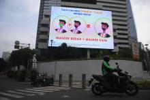 A motorcyclist crosses a digital banner showing health protocol information in Jakarta on January 17, 2022. ANTARA FOTO/Akbar Nugroho Gumay/wsj.